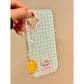 Phone case with a checkered pattern, pink dog charm, and yellow tag held by a hand on a beige background.