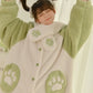A person wearing a plush fleece pajama set in light green and off-white, featuring paw print details on the front and cuffs, with a matching headband visible at the top.