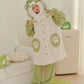 A person wearing a plush animal-themed pajama set with a hooded long-sleeve top and matching pants in light green and off-white, featuring paw print details, standing in a bright indoor room.