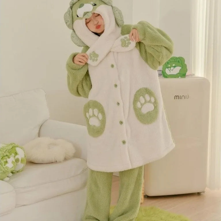 A person wearing a plush animal-themed pajama set with a hooded long-sleeve top and matching pants in light green and off-white, featuring paw print details, standing in a bright indoor room.