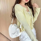 Woman wearing a light yellow cardigan holding a white heart shaped handbag.