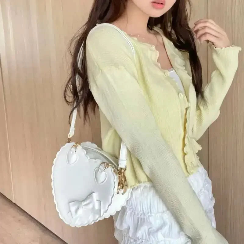 Woman wearing a light yellow cardigan holding a white heart shaped handbag.