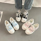 cute cat shoes with cartoon designs worn by a person sitting on a couch.