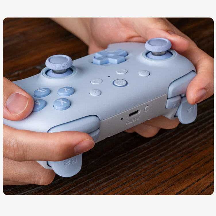 Light blue gaming controller held in hands on a wooden surface