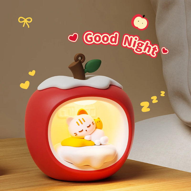 Decorative night light shaped like a red apple with Kawaii characters inside, on a wooden surface.