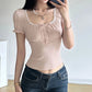 Woman wearing a beige top with lace details and blue jeans indoors.