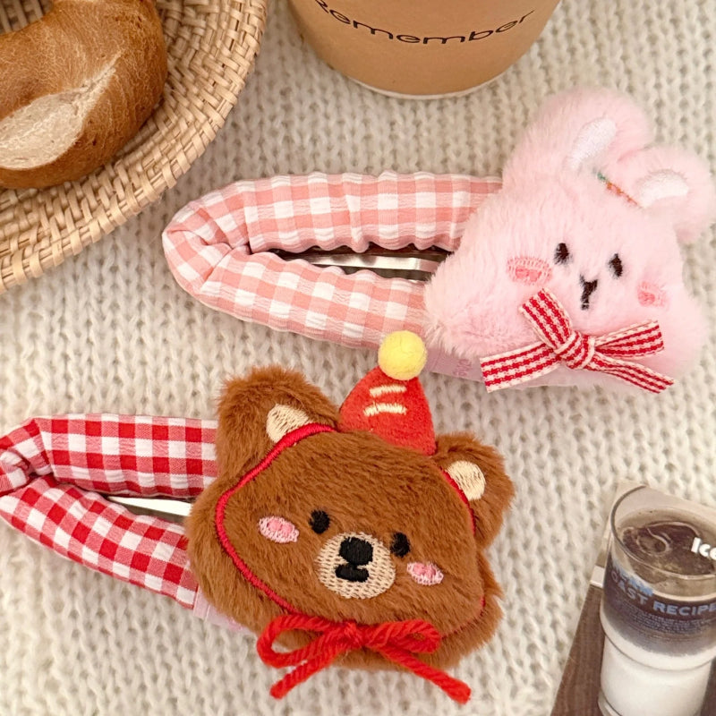 Cute plush brown bear hair clip with checkered red pattern and a pink bunny hair clip with checkered pink pattern on a textured surface.