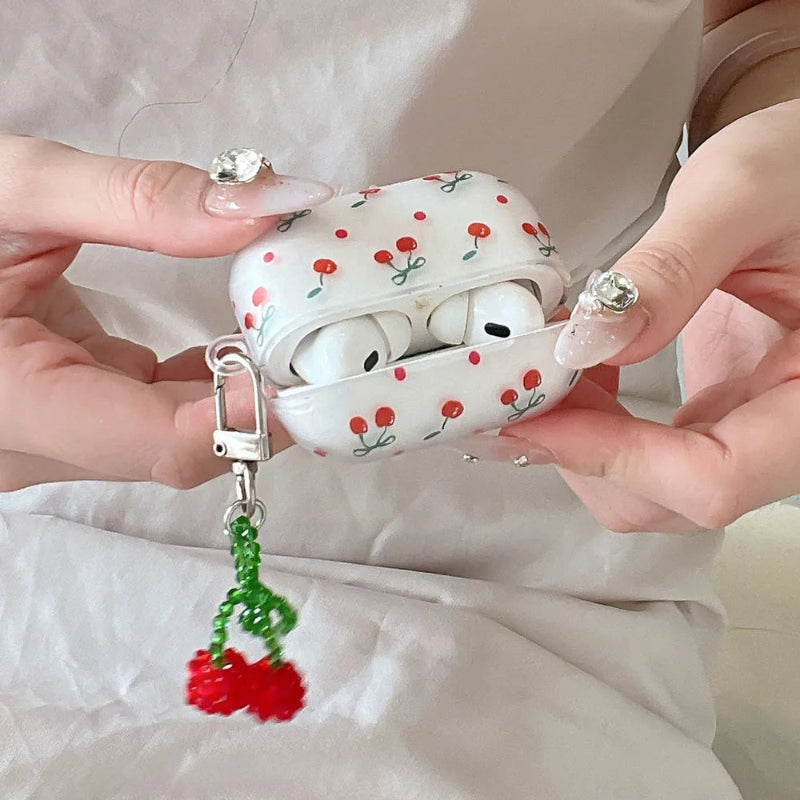 White airpod case with red cherry design held by hands with decorative nails.