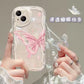 Phone case with butterfly design held by a person, featuring a decorative chain. the butterfly on the case is a subtle pink.
