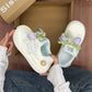 White sneakers with decorative elements held by a person in front of an open box.