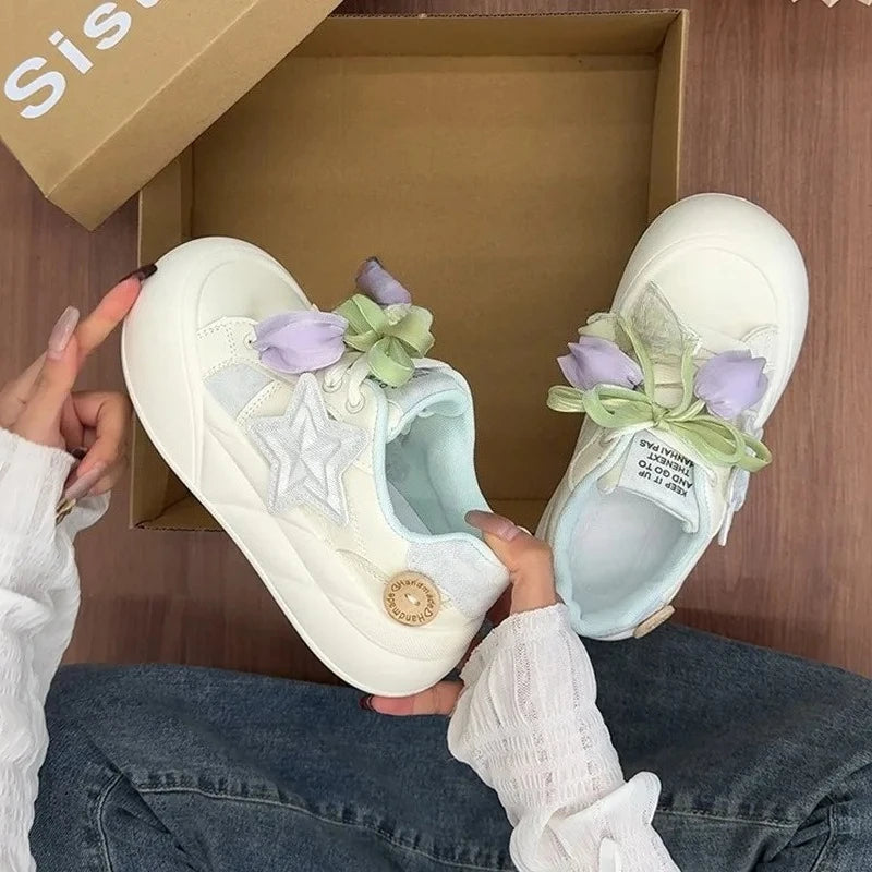 White sneakers with decorative elements held by a person in front of an open box.