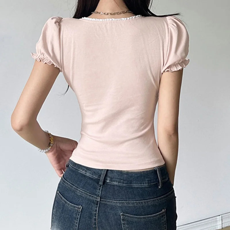 Person wearing a light pink top with puffed sleeves and dark blue jeans against a plain background