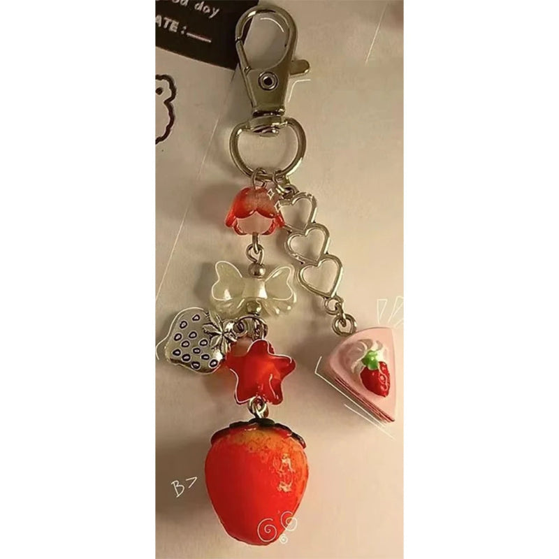 Strawberry-themed keychain with heart and bow charms on a beige background