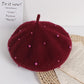 Dark Red beret with pink beads on a white surface with text and paper.