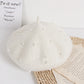 White beret with pearl embellishments on a white surface with text and paper.