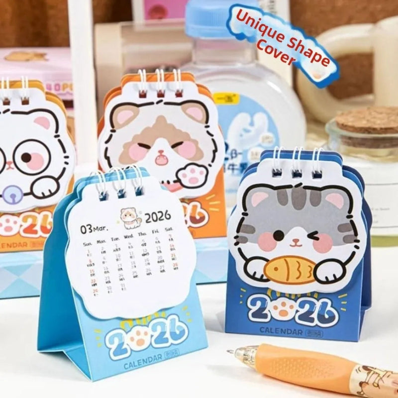 Set of kawaii cat-themed desk calendars with a pen on a surface.