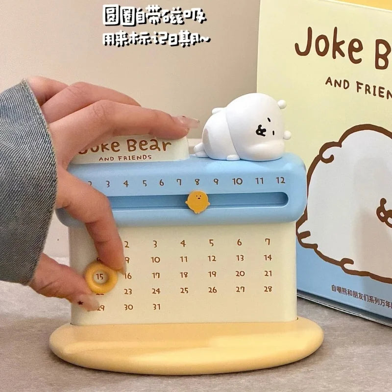 Calendar with a bear figurine on top, held by a hand, with 'Joke Bear' branding in the background.