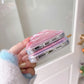 Stack of pink glittery phone cases held by a person with a blurred indoor background