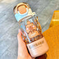 Clear water bottle with capybara design held by a hand on a wooden surface.