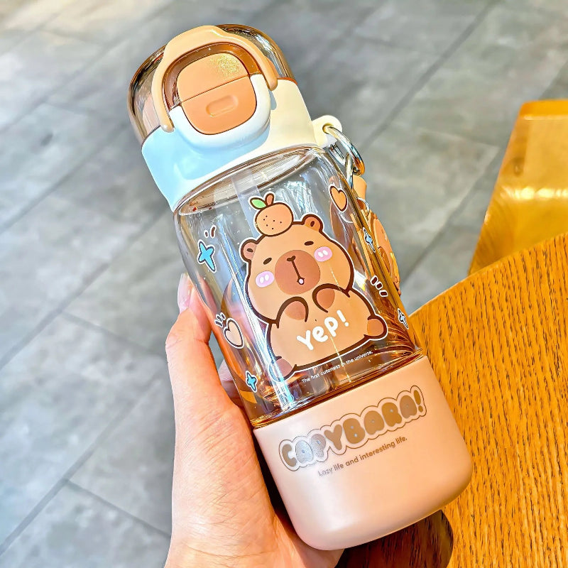Clear water bottle with capybara design held by a hand on a wooden surface.