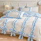 White duvet cover with Blue bows and ribbons on a bed in a bedroom setting.