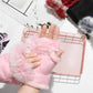Pink fluffy fingerless gloves worn on a hand with a white background