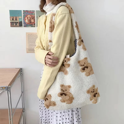 Person holding a white tote bag with brown teddy bear patterns in a room.