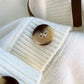 Sweet Teddy Bear Cardigan white edition with a bear sown into the chest area whilst the sleeves have large black stitches where they have been joined and black strips on the wrist cuffs and black and white trim, this picture is showing a close up of the button which is dappled beige and black.