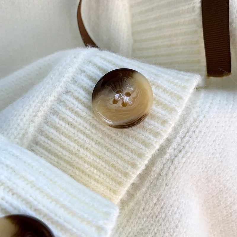 Sweet Teddy Bear Cardigan white edition with a bear sown into the chest area whilst the sleeves have large black stitches where they have been joined and black strips on the wrist cuffs and black and white trim, this picture is showing a close up of the button which is dappled beige and black.