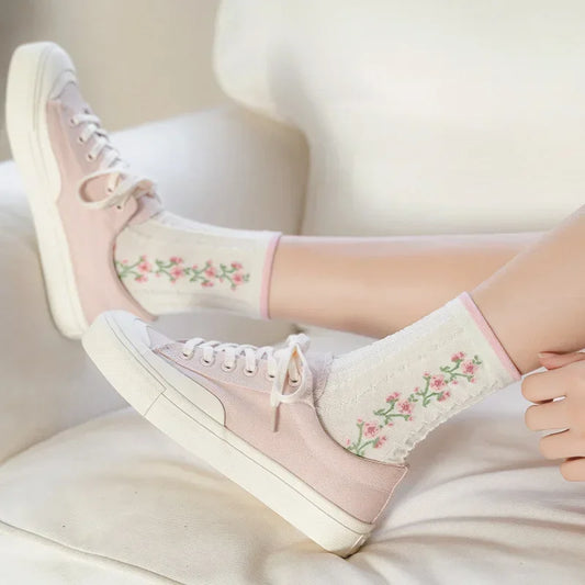 Person wearing pink sneakers with floral embroidery socks on a white background