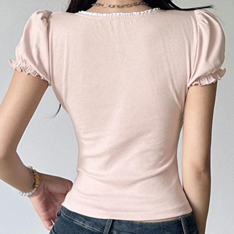 Person wearing a light pink top with ruffled sleeves and blue jeans on a plain background