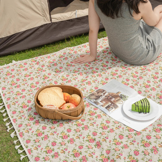 Person sitting on a floral picnic blanket with a basket of food and a plate of fruit.
