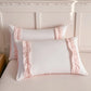 Two white pillows with pink ruffle edges on a bed.