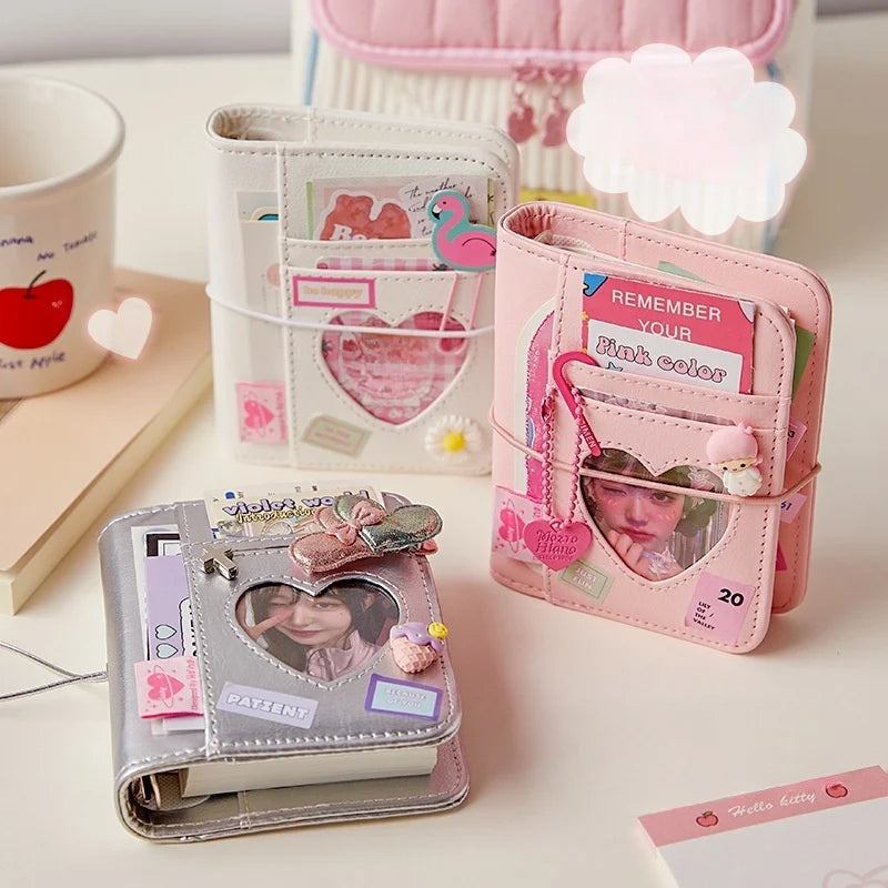 White, Silver, and Pink mini Albums with heart cutout on a desk with a cup.