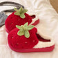 Red strawberry-shaped slippers with green leaves on a soft white surface.