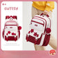 Red and white backpack with decorative elements held by a person, on a light pink background.