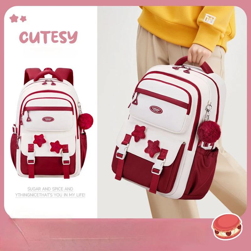 Red and white backpack with decorative elements held by a person, on a light pink background.