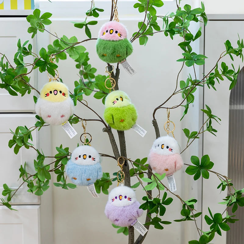 Colorful cute bird stuffed animal keychains  hanging from a branch with green leaves.