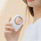 Person holding a small white cooling device with a shiba inu character on a beige background.