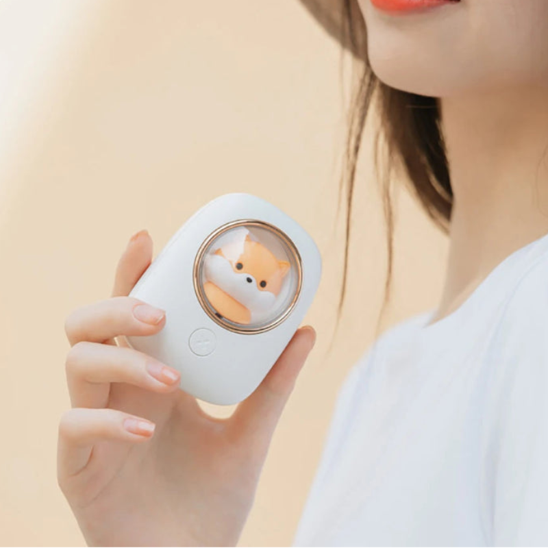 Person holding a small white cooling device with a shiba inu character on a beige background.
