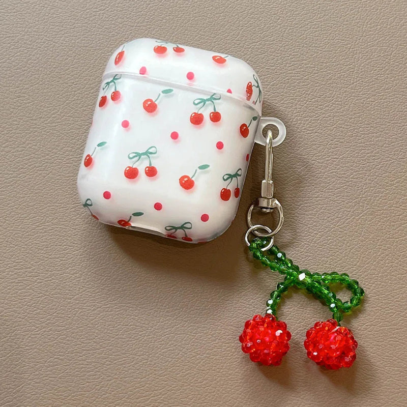 White AirPods case with cherry pattern and red cherry charm on beige background