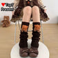 A person seated on a chair wearing dark brown ribbed leg warmers with teddy bear head embellishments and brown bow shoes. The photo is cropped from the waist down, with a small teddy bear toy visible on the floor in the background.