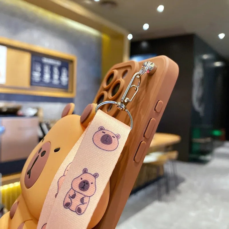 Phone case with cartoon capybara design and strap in a blurred indoor setting