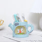 Cute blue watering can-shaped pen holder with cartoon animals on a white surface.