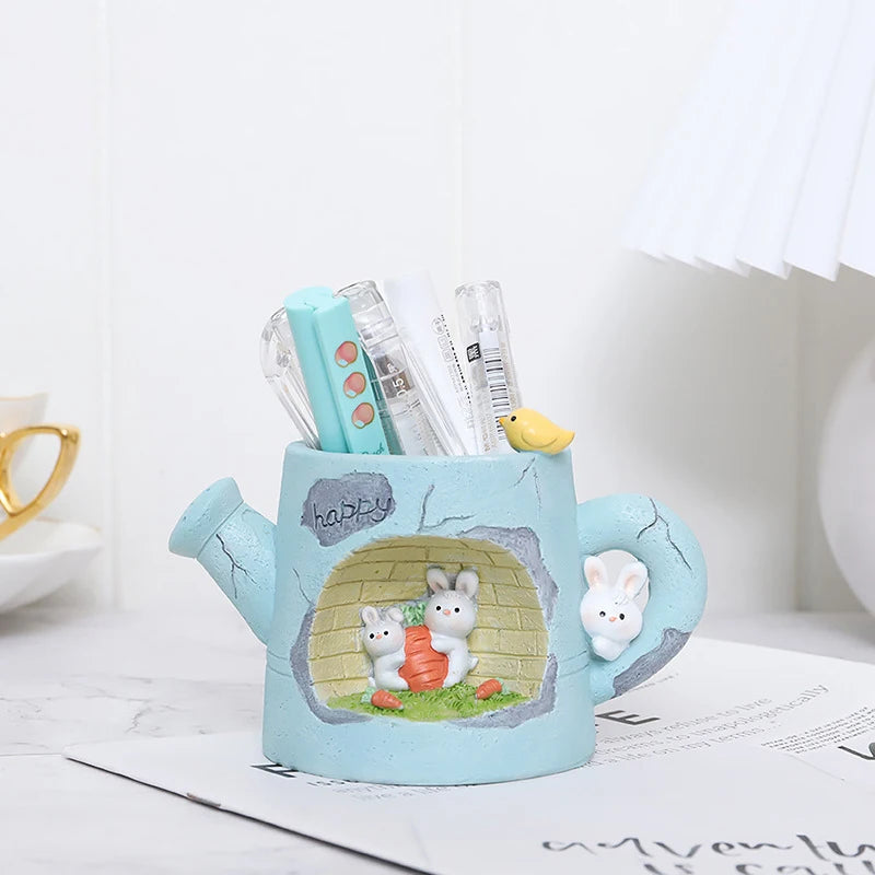 Cute blue watering can-shaped pen holder with cartoon animals on a white surface.