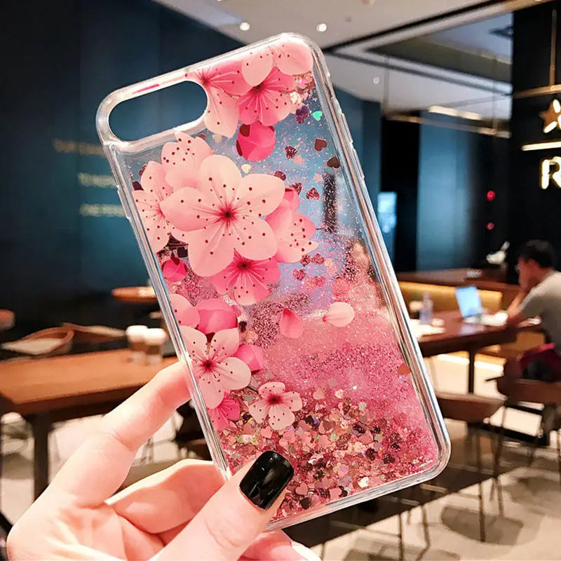 Phone case with pink sakura design held in a hand, indoor setting