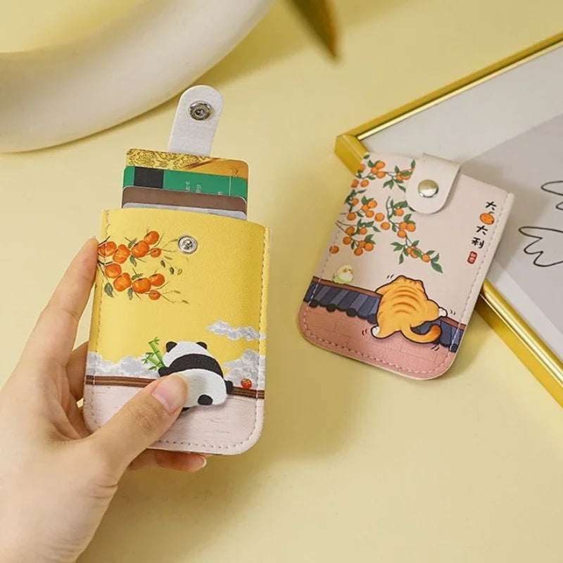 Two cartoon-themed card holders on a yellow surface with a hand holding one of them.