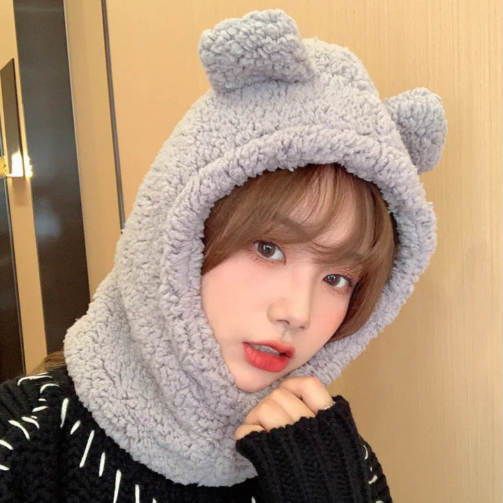 Person wearing a gray fleece hat with bear ears against a beige wall.