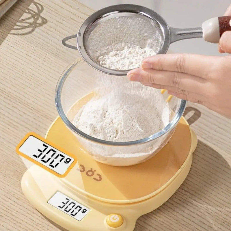 Person sifting flour into a bowl on a kawaii digital kitchen scale.
