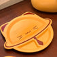 A yellow cat-shaped divided plate with dark red accents, shown on a dark brown wooden tabletop.